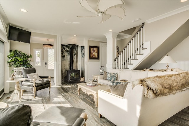 living room with crown molding, a wood stove, a decorative wall, wood finished floors, and ornate columns