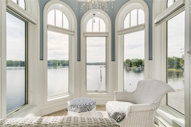 sunroom with carpet, a water view, and a notable chandelier