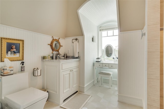 bathroom featuring vanity, lofted ceiling, and a wainscoted wall