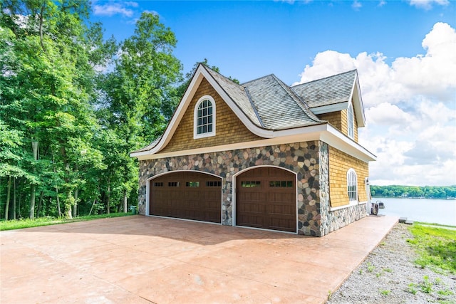 view of side of home featuring a water view, stone siding, and concrete driveway