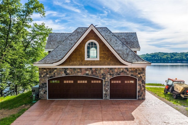 view of front of home with a water view, driveway, stone siding, and a garage