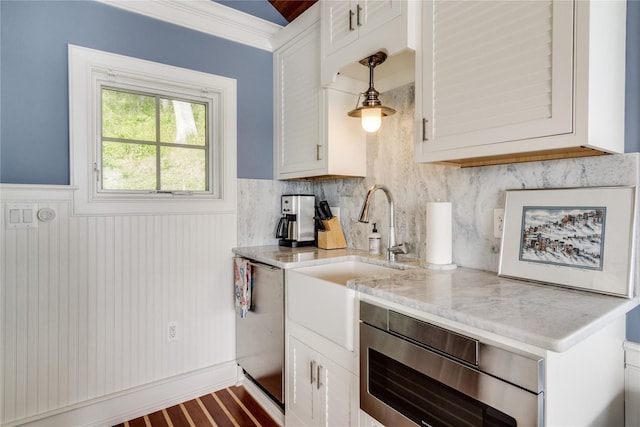 kitchen with decorative backsplash, appliances with stainless steel finishes, wainscoting, a sink, and white cabinets