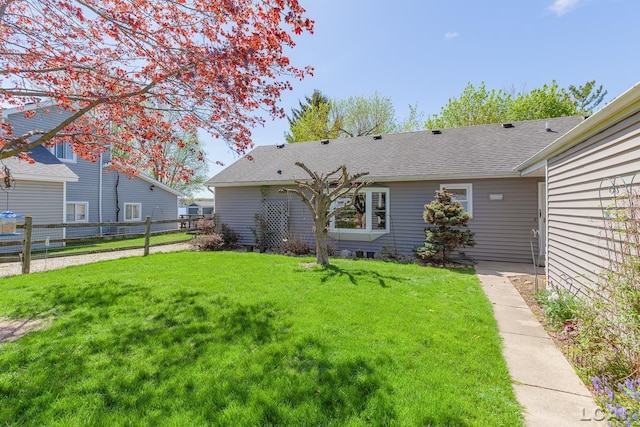 rear view of property featuring a yard, fence, and a shingled roof
