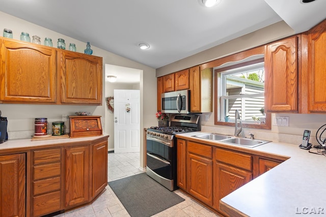 kitchen with light countertops, stainless steel appliances, brown cabinetry, and a sink