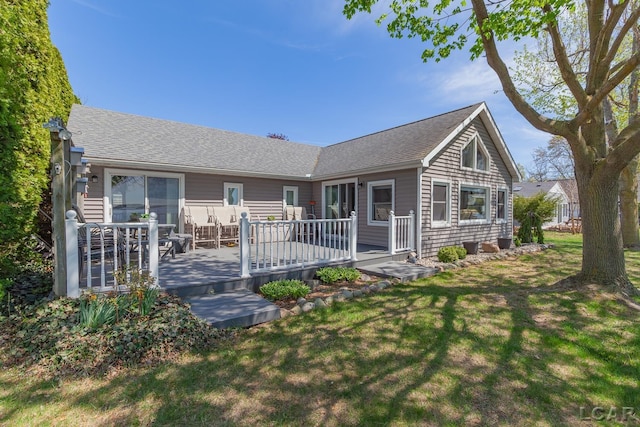 back of property with a lawn, a deck, and a shingled roof
