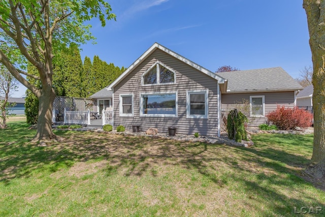 back of house with roof with shingles, a wooden deck, and a yard