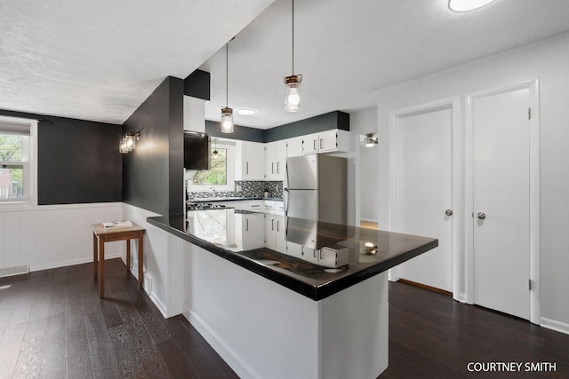 kitchen with freestanding refrigerator, a peninsula, dark countertops, and dark wood-type flooring