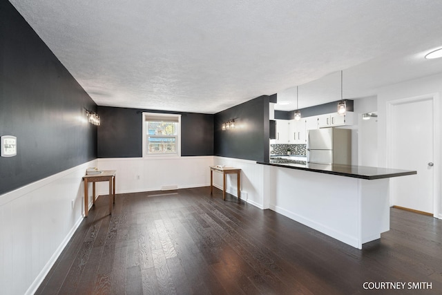 kitchen with freestanding refrigerator, dark countertops, dark wood finished floors, and a wainscoted wall
