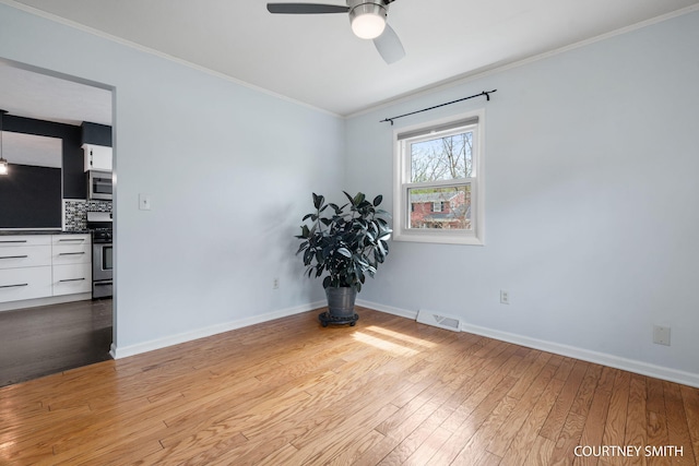 spare room featuring a ceiling fan, visible vents, crown molding, baseboards, and hardwood / wood-style floors