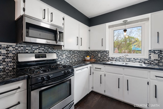 kitchen featuring decorative backsplash, appliances with stainless steel finishes, dark countertops, a sink, and white cabinetry