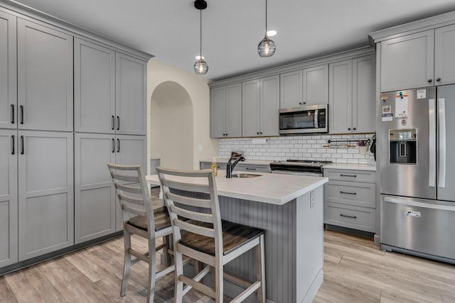 kitchen with backsplash, stainless steel appliances, arched walkways, and gray cabinetry