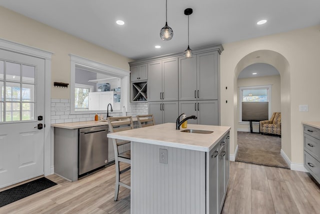 kitchen featuring gray cabinets, tasteful backsplash, a sink, light wood finished floors, and dishwasher