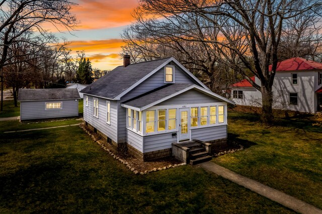 rear view of house featuring a sunroom, a yard, a chimney, and roof with shingles
