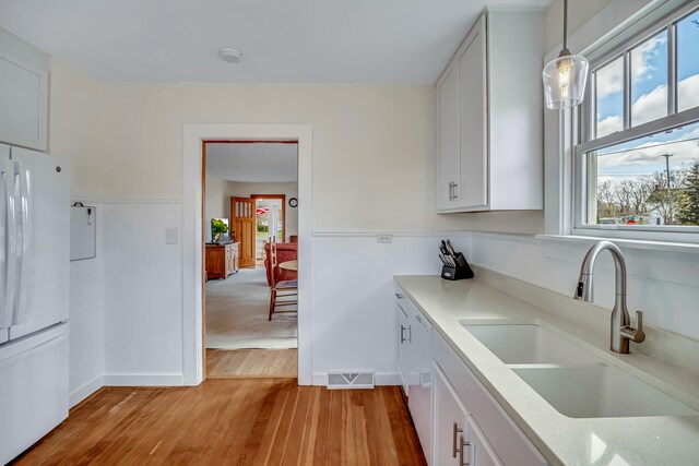 kitchen featuring freestanding refrigerator, white cabinetry, a sink, and light wood-style floors