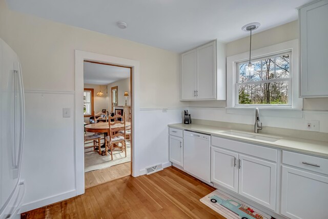 kitchen with a sink, white appliances, light wood-style flooring, white cabinetry, and visible vents