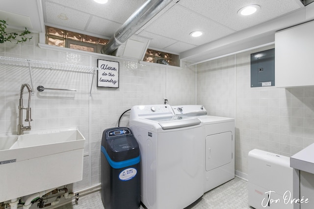 clothes washing area featuring electric panel, laundry area, tile walls, a sink, and washer and clothes dryer