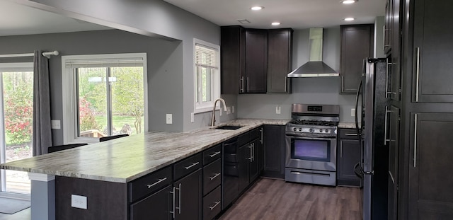 kitchen with a peninsula, dark wood-style floors, wall chimney exhaust hood, a sink, and stainless steel appliances