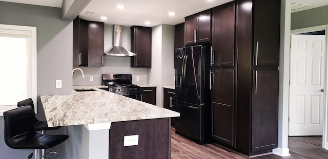 kitchen with wall chimney range hood, a sink, a breakfast bar area, a peninsula, and black appliances