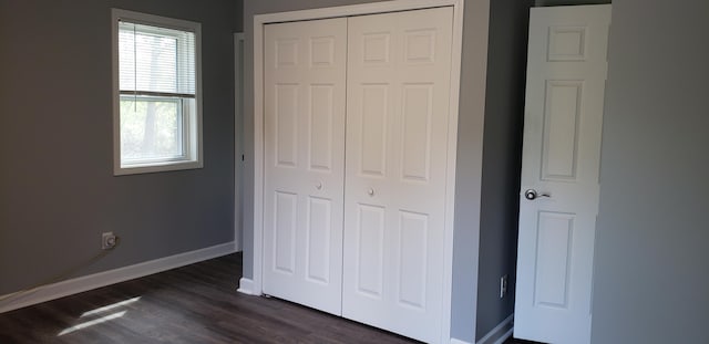 unfurnished bedroom featuring dark wood-style flooring, baseboards, and a closet