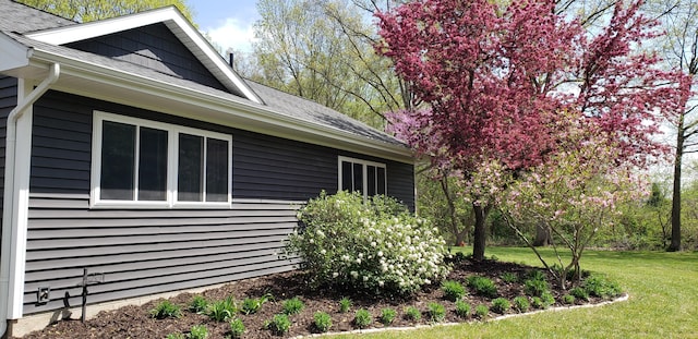 view of side of property featuring a shingled roof and a yard