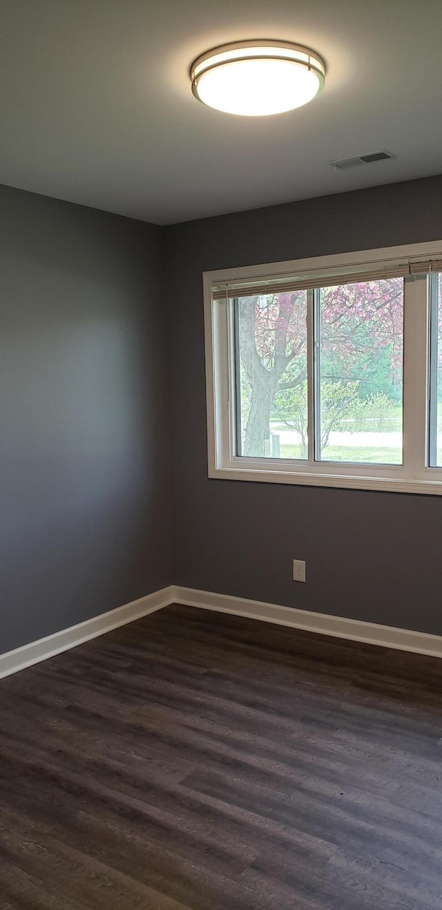 unfurnished room with visible vents, baseboards, a wealth of natural light, and dark wood-style floors
