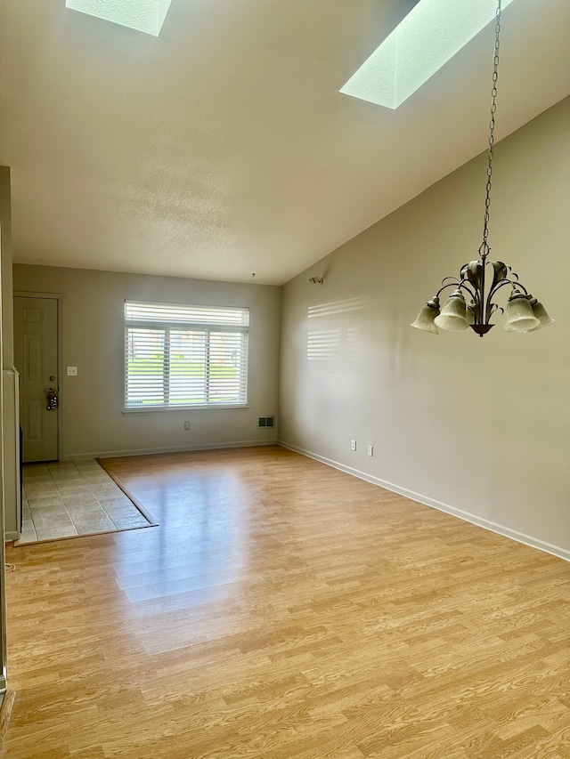 empty room featuring light wood-type flooring, baseboards, lofted ceiling with skylight, and a chandelier