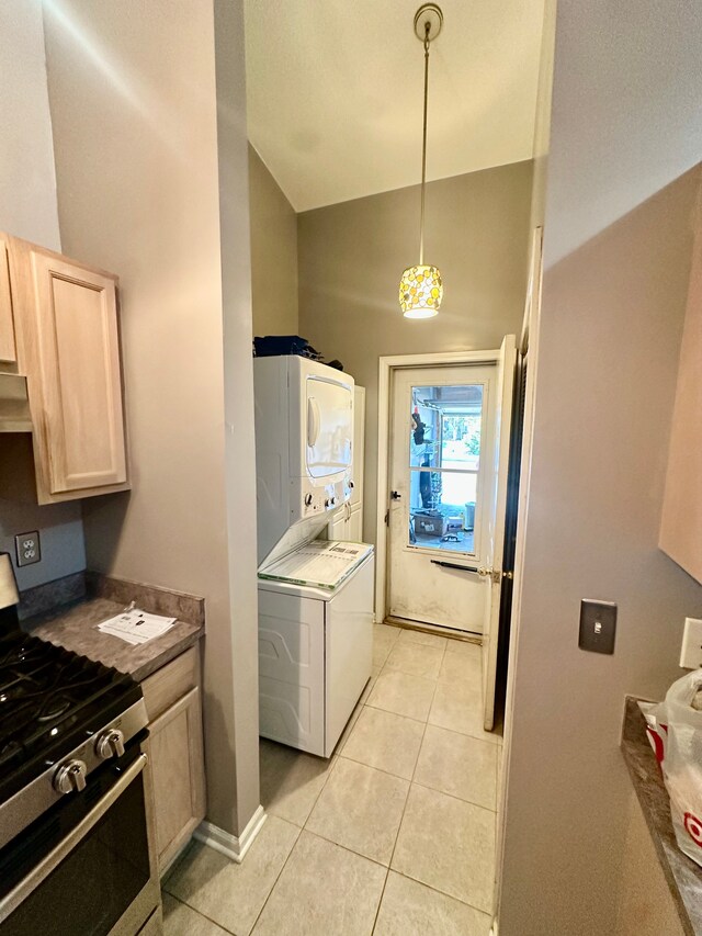 kitchen featuring stacked washer / dryer, light brown cabinetry, stainless steel gas stove, light tile patterned floors, and high vaulted ceiling