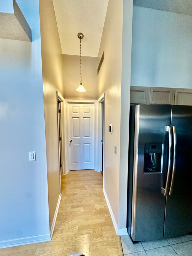 hallway featuring baseboards, visible vents, light wood-style flooring, and a towering ceiling