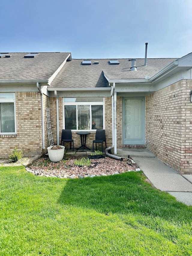 doorway to property with brick siding, roof with shingles, and a yard