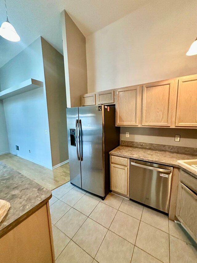 kitchen featuring light brown cabinetry, stainless steel appliances, light tile patterned floors, lofted ceiling, and pendant lighting