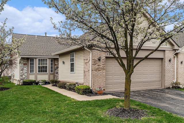 view of front of house with aphalt driveway, roof with shingles, brick siding, a garage, and a front lawn