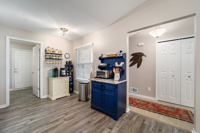 kitchen featuring lofted ceiling, baseboards, visible vents, blue cabinetry, and light wood-type flooring