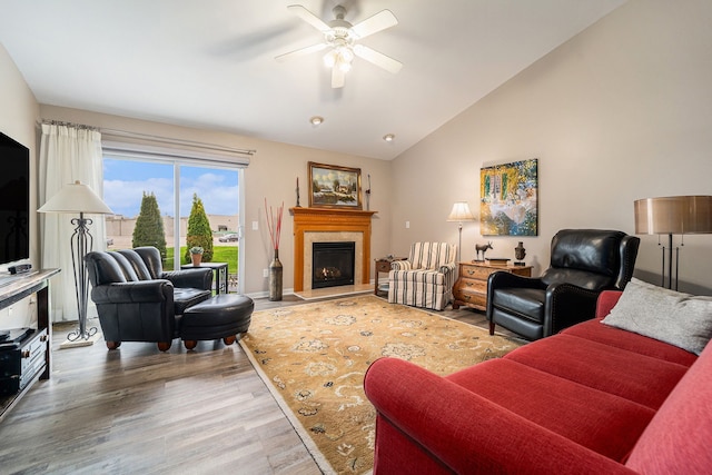 living room featuring vaulted ceiling, wood finished floors, ceiling fan, and a lit fireplace