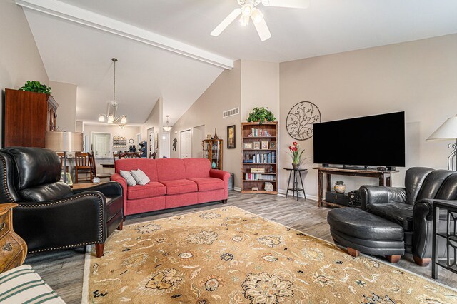 living room with baseboards, visible vents, ceiling fan with notable chandelier, wood finished floors, and lofted ceiling with beams