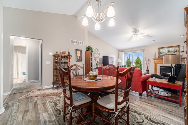 dining room featuring ceiling fan with notable chandelier, wood finished floors, visible vents, vaulted ceiling, and baseboards