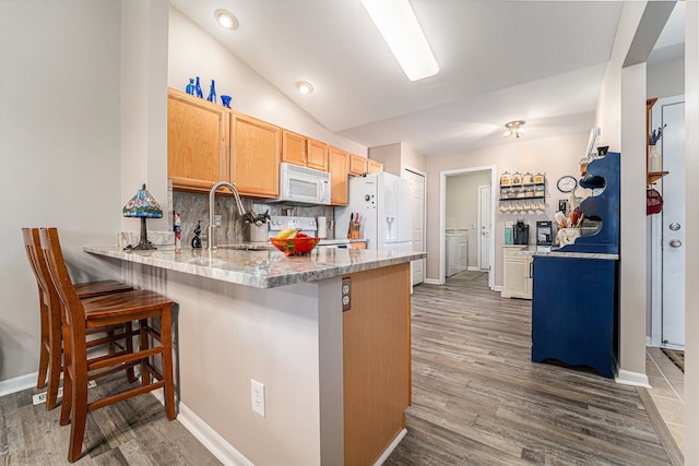 kitchen featuring a sink, a peninsula, white appliances, washer / dryer, and wood finished floors