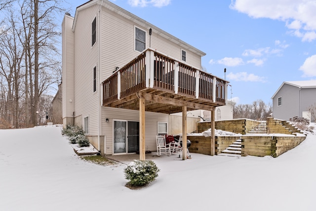 snow covered rear of property with a wooden deck and a patio