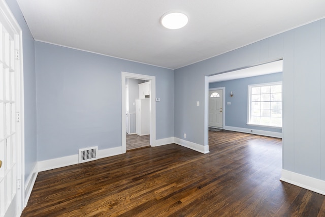 empty room featuring baseboards, visible vents, and dark wood-style floors