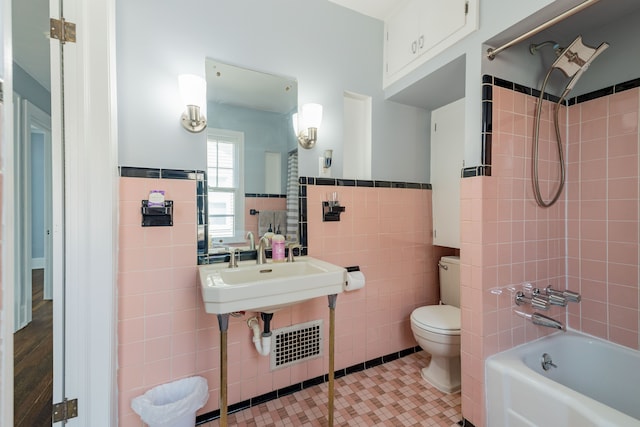bathroom with tile patterned flooring, wainscoting, bathing tub / shower combination, toilet, and tile walls
