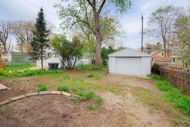 view of yard with fence, a detached garage, an outbuilding, and driveway