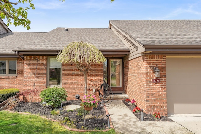 doorway to property with roof with shingles, a garage, and brick siding