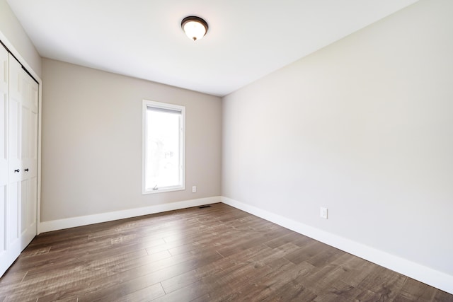 unfurnished bedroom featuring dark wood-style flooring, baseboards, and a closet