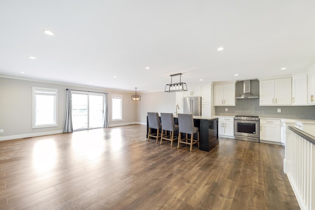 kitchen with open floor plan, dark wood-style floors, wall chimney exhaust hood, white cabinetry, and stainless steel appliances