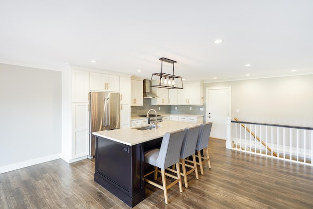 kitchen with high end fridge, ornamental molding, wall chimney exhaust hood, and light countertops