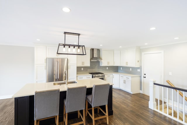 kitchen with a kitchen island with sink, backsplash, a sink, stainless steel appliances, and wall chimney exhaust hood