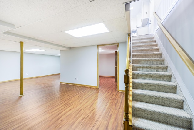 finished basement with baseboards, stairs, wood finished floors, and a drop ceiling