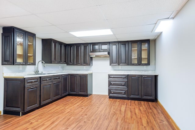 bar with under cabinet range hood, a drop ceiling, a sink, and light wood-type flooring