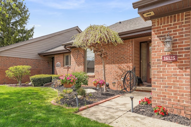 entrance to property with roof with shingles, a yard, and brick siding