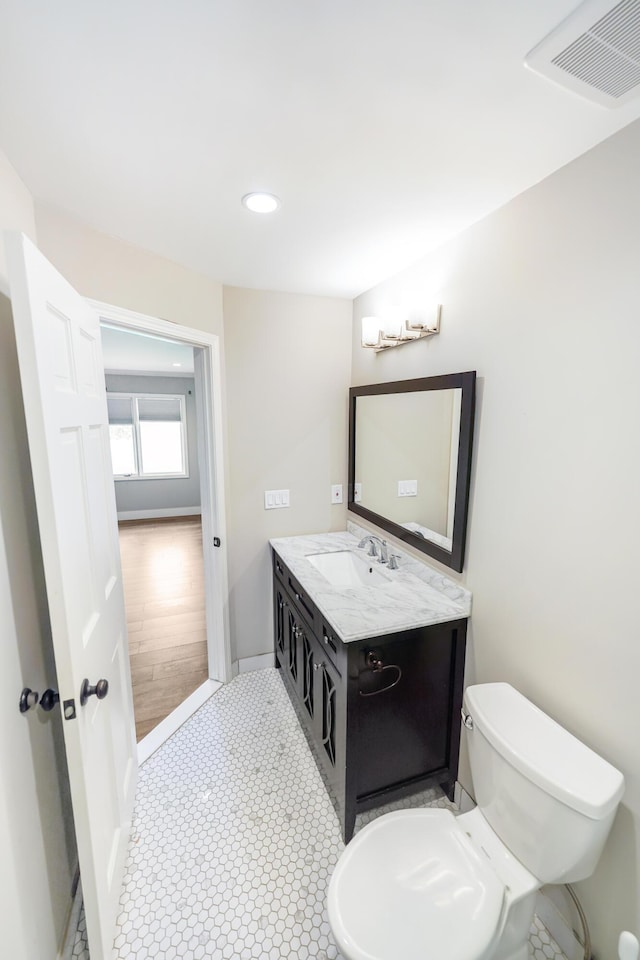 half bathroom with visible vents, vanity, toilet, baseboards, and recessed lighting