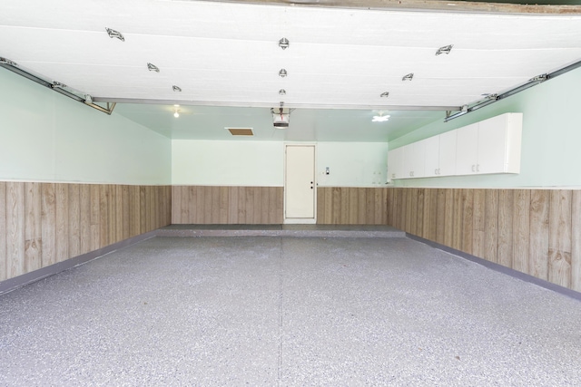 garage with wood walls, a garage door opener, and a wainscoted wall